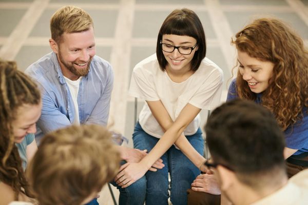 A diverse group of people smiling and sitting in a relaxed posture in a bright, welcoming space.