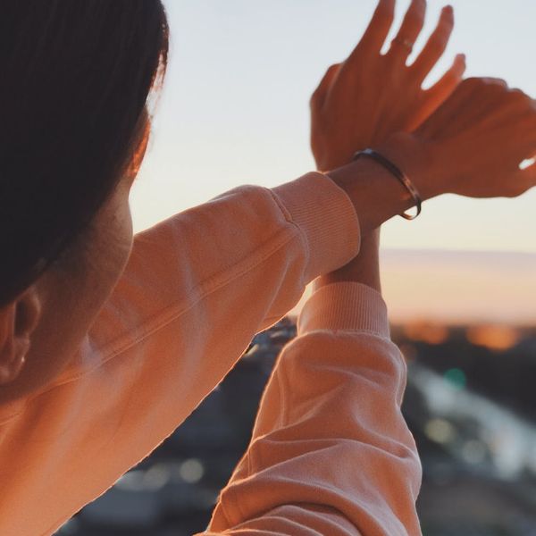 A person viewed from behind, stretching their arms towards a sunrise over a calm lake, feeling serene.